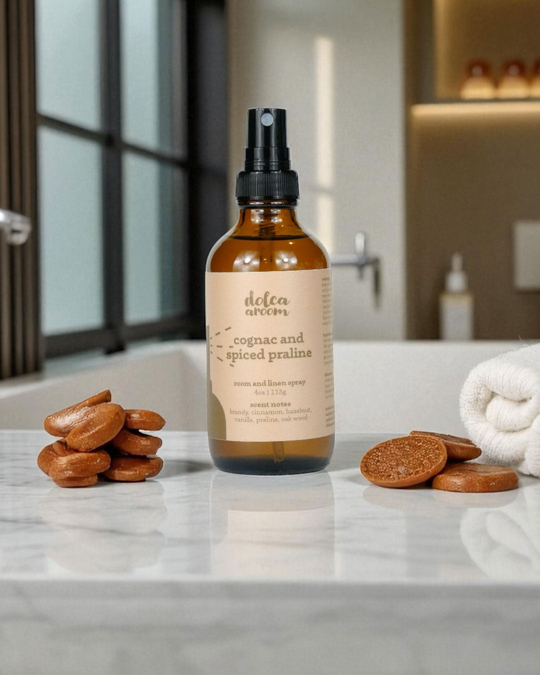 dolca aroom 4oz room and linen spray, cognac and spiced praline scent on a marble surface with cookies.