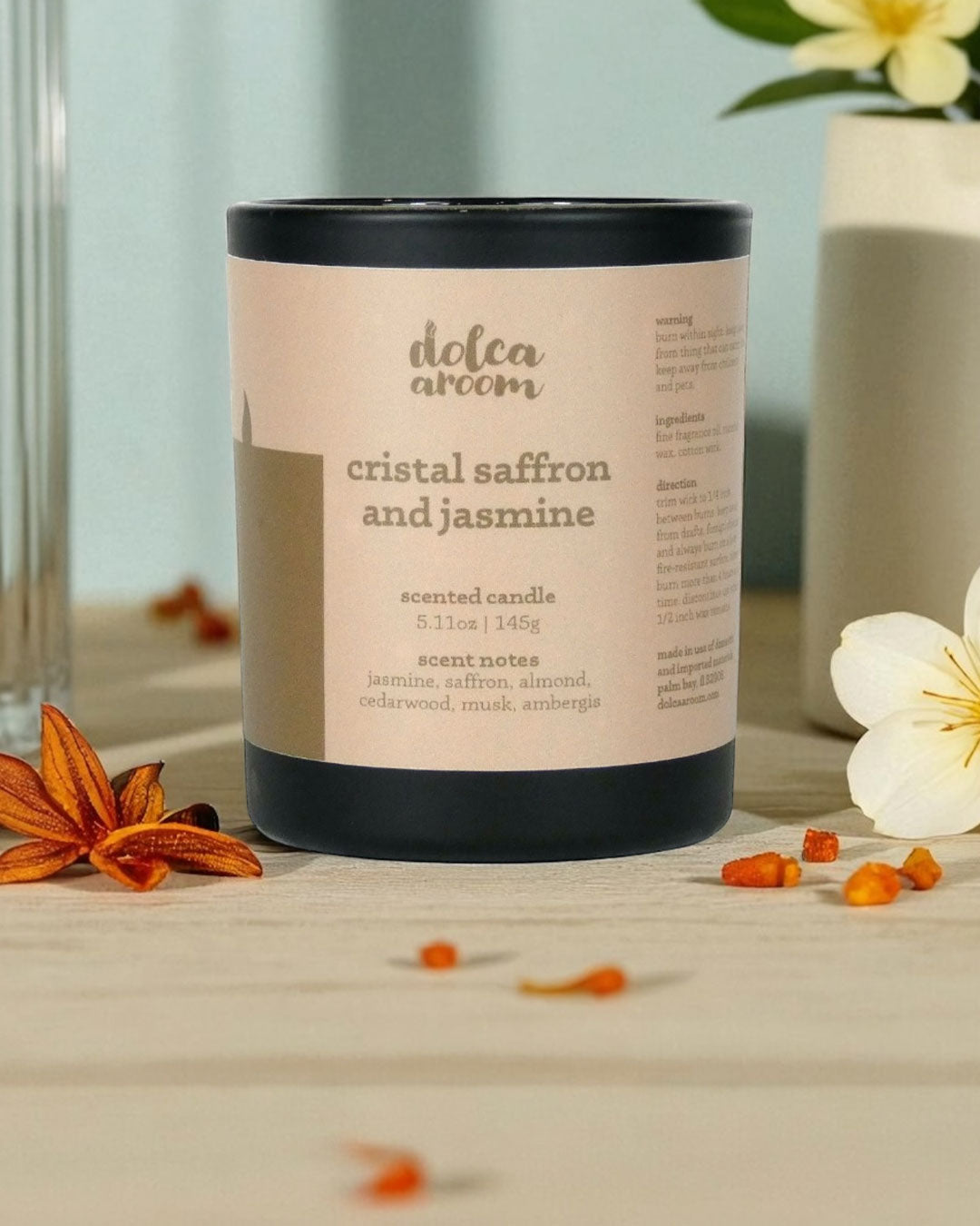 dolca aroom 5.11oz scented candle, cristal saffron and jasmine scent with saffron and jasmine flowers on a wooden surface.