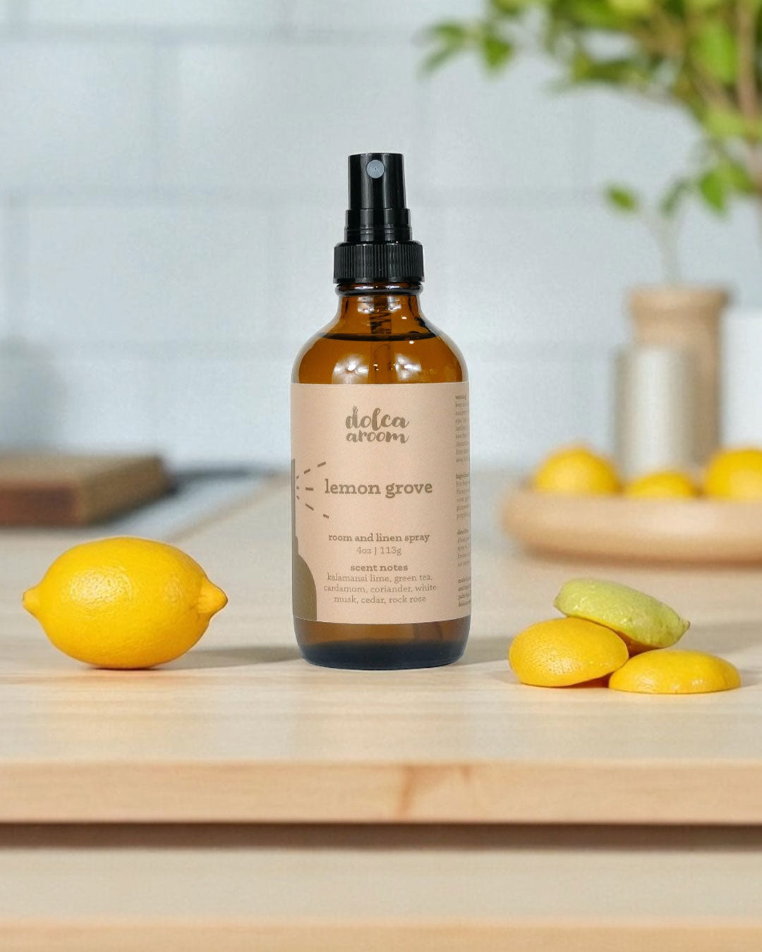 dolca aroom 4oz room and linen spray, lemon grove scent on a wooden surface with lemons and a blurred background