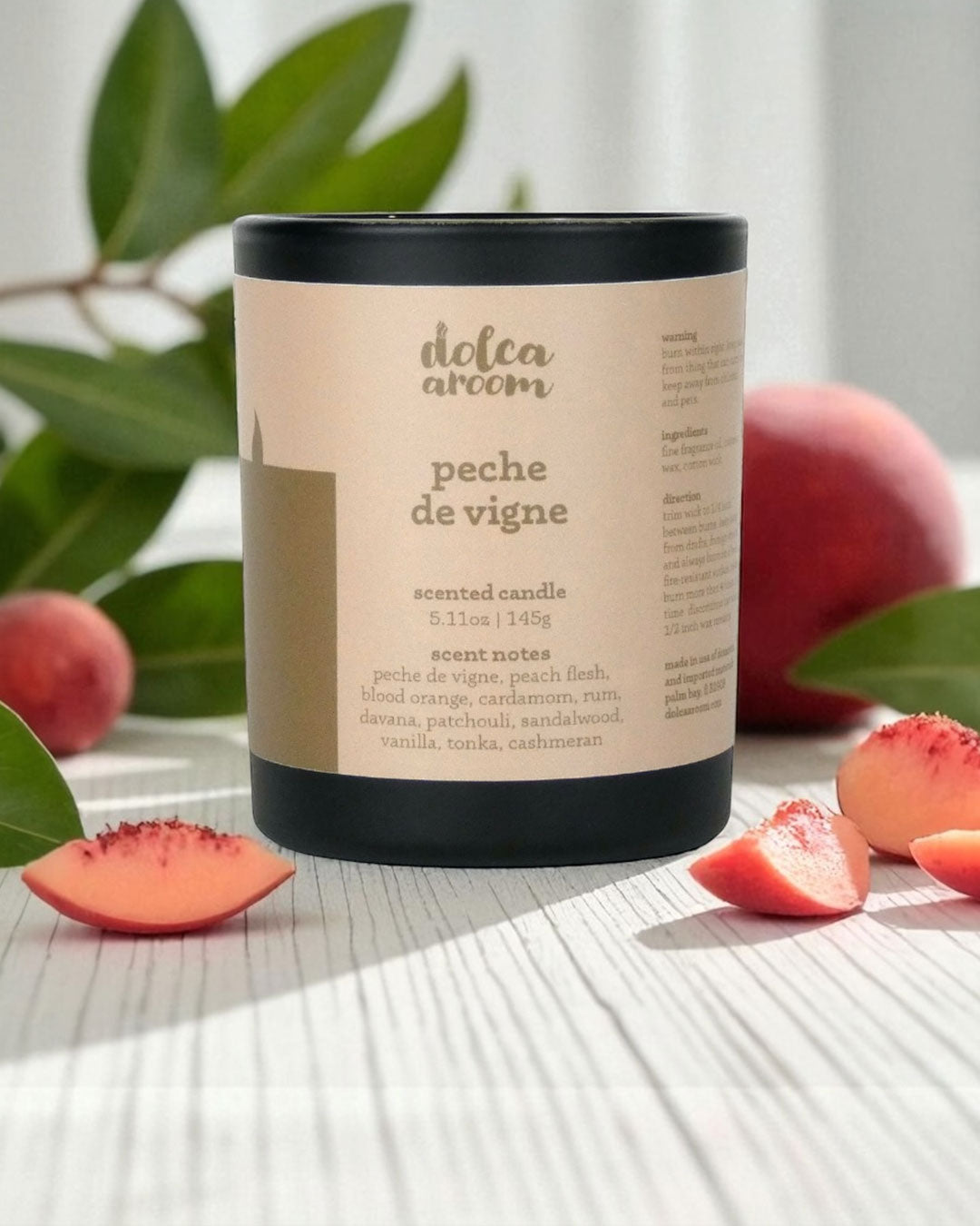 dolca aroom 5.11oz scented candle, peche de vigne scent with peaches and leaves on a light surface