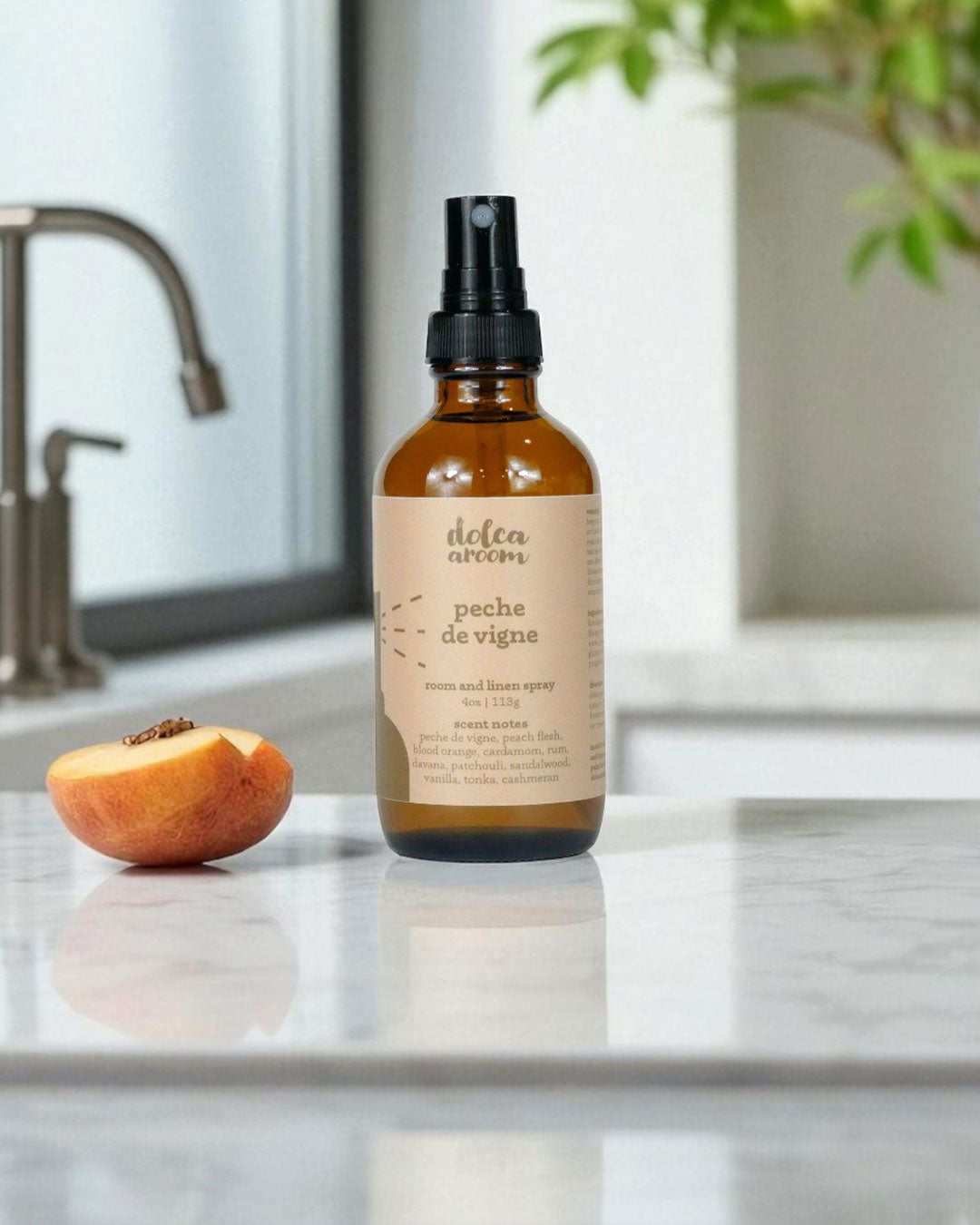 dolca aroom 4oz room and linen spray, peche de vigne scent on a kitchen counter with a peach and window in the background.